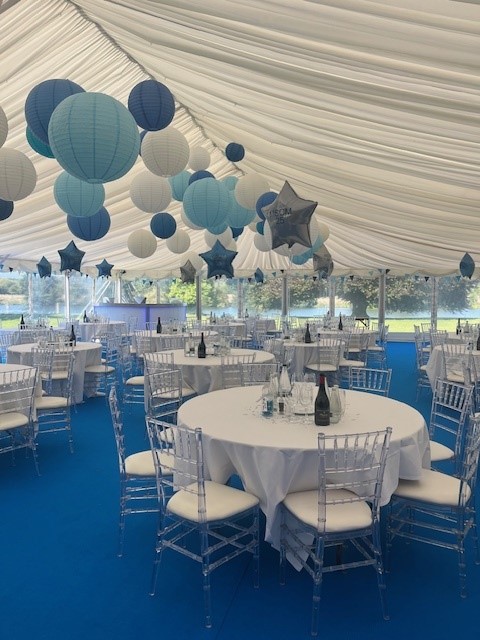 Interior of the anniversary marquee with blue and white lanterns and round tables overlooking the grounds
